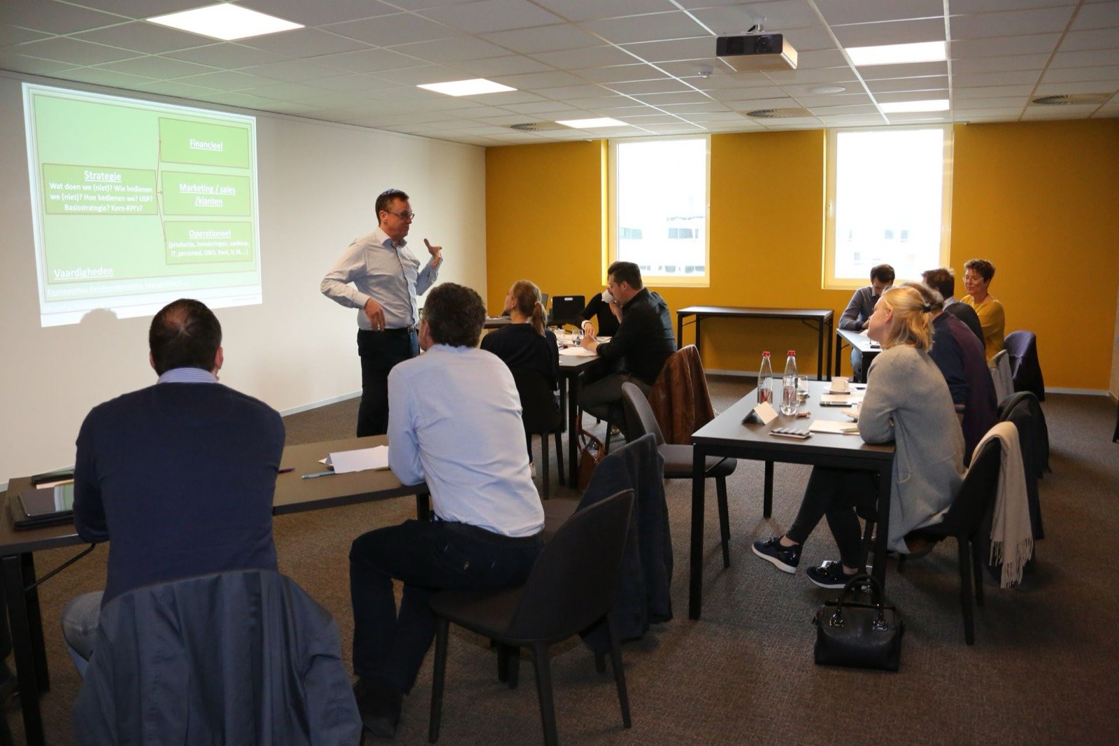 Kurt Vandewalle presenteert voor een groep bedrijfsleiders in een workshopruimte